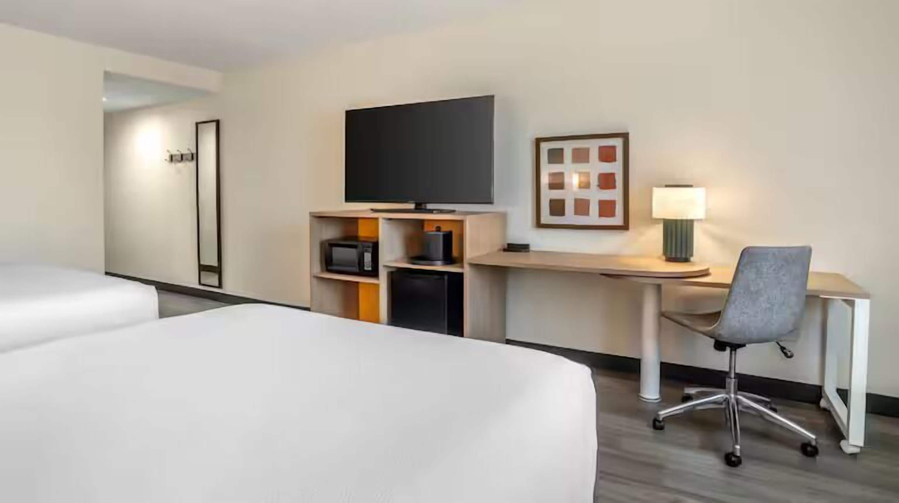 A hotel room with two beds, a desk with a computer, a television, and a lamp.