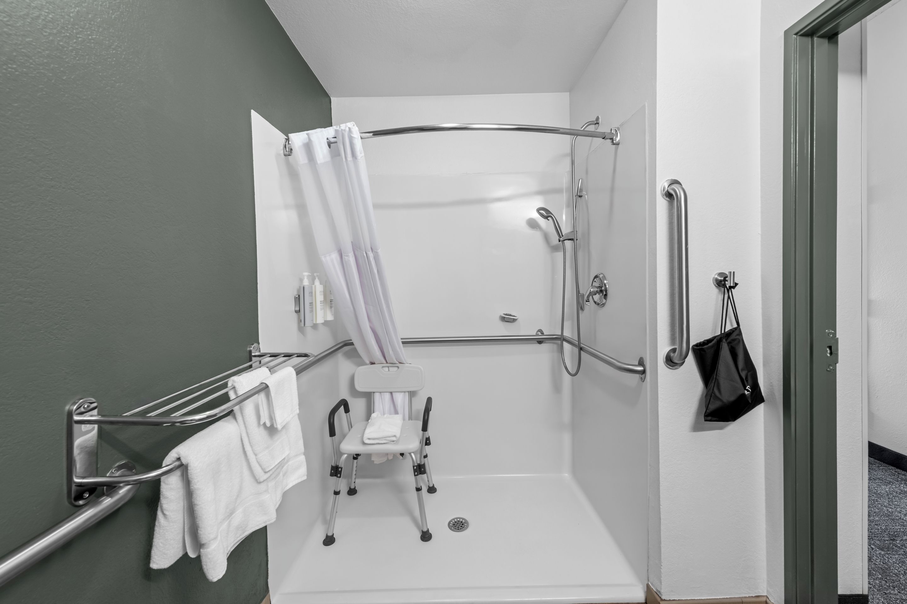A wheelchair-accessible shower with a grab bar, a towel rack, and a small step stool.