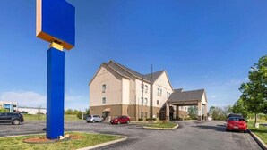 Un hôtel avec une grande enseigne bleue, un parking où sont garées plusieurs voitures et un bâtiment à la façade beige.