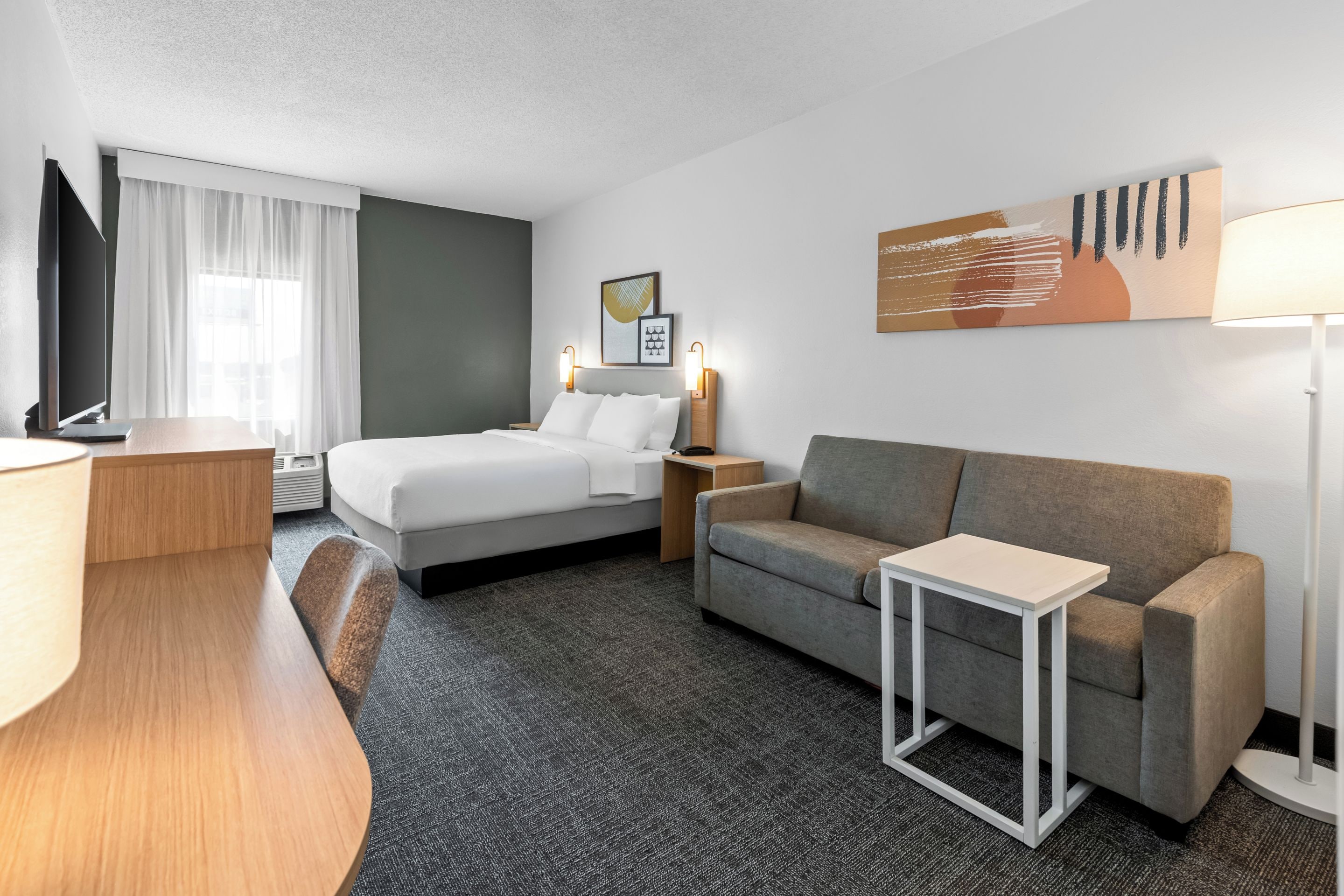 Habitación de hotel con cama, sofá, escritorio, televisión y lámpara.