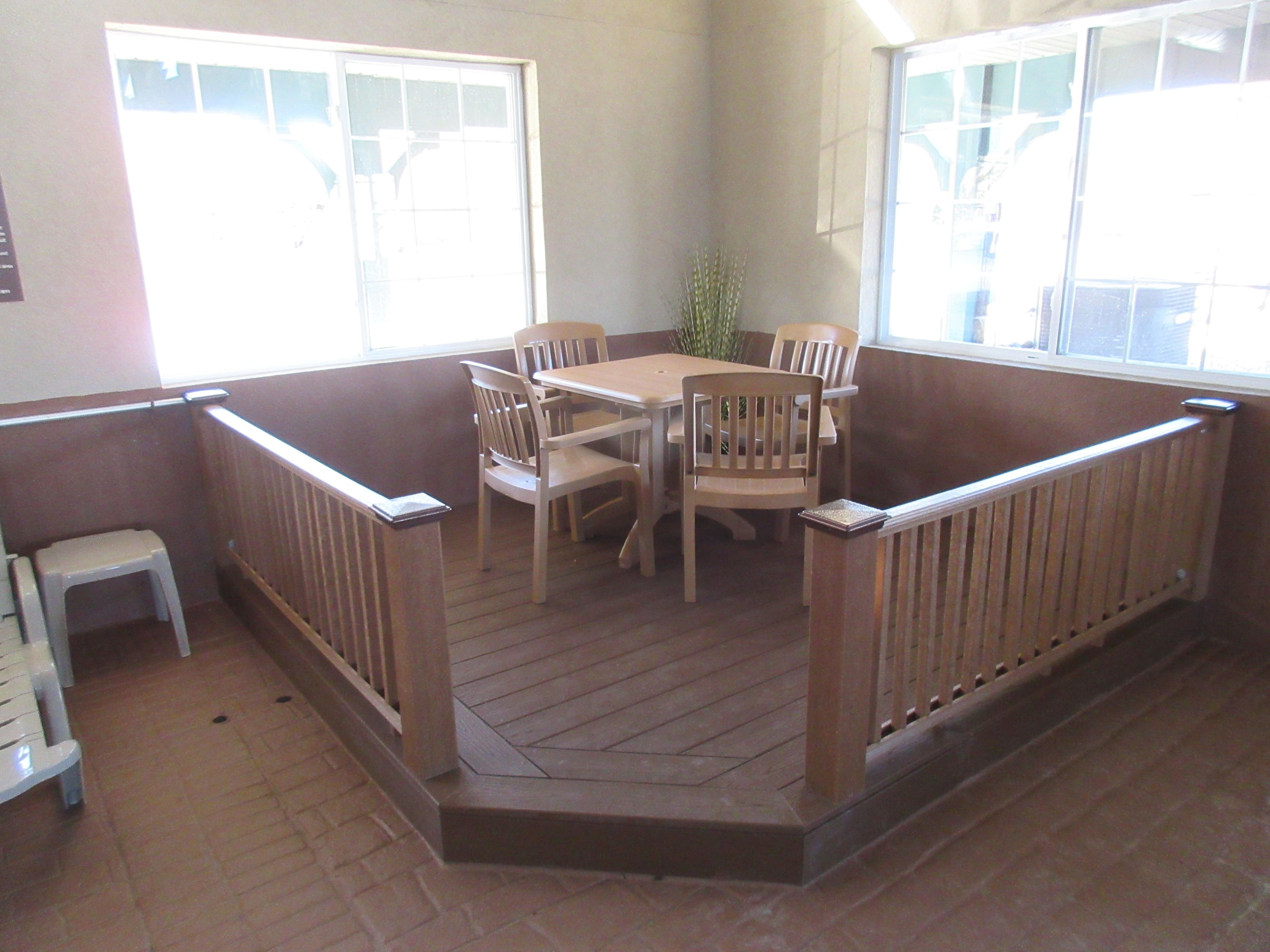Una habitación luminosa con una terraza de madera, una mesa de comedor con sillas y un taburete blanco pequeño.