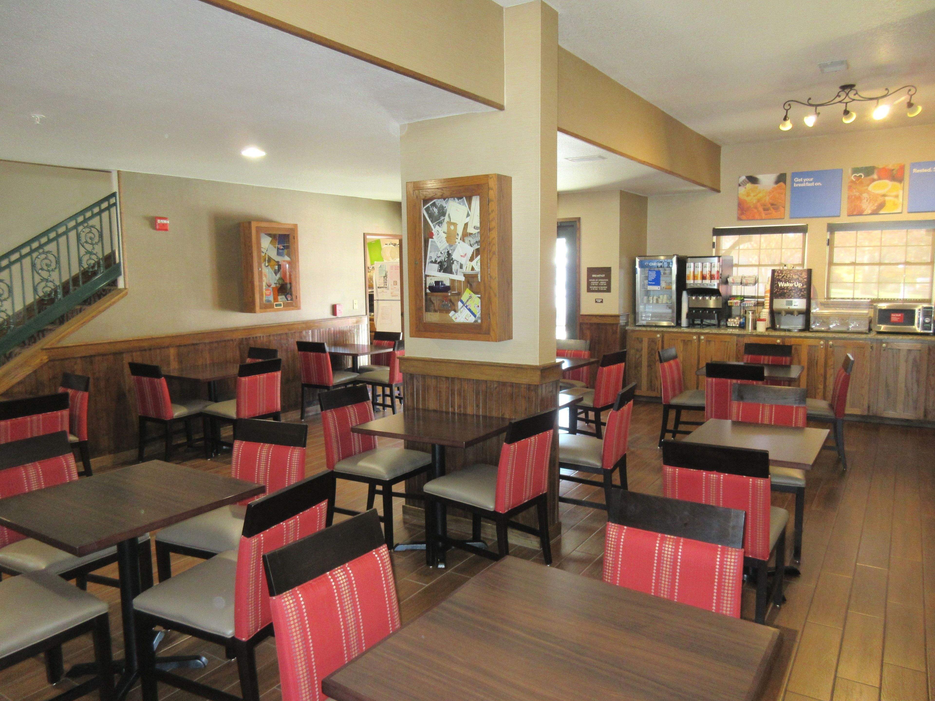A restaurant with multiple tables and chairs, a staircase, and a kitchen area.