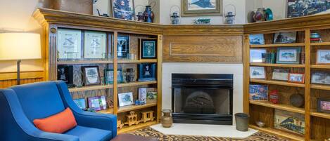 Une bibliothèque avec des étagères, une cheminée, un fauteuil bleu et un tapis à motifs.
