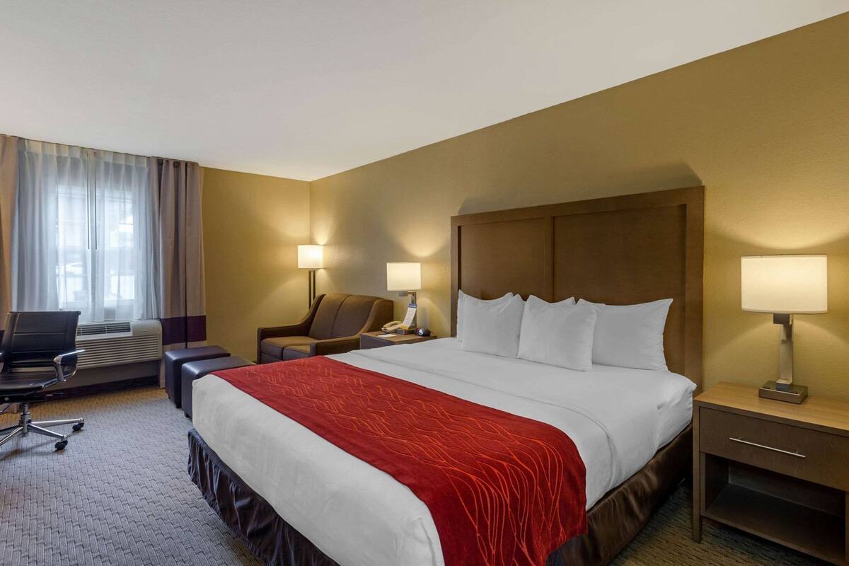 Habitación de hotel con una cama grande, dos lámparas de noche, un escritorio con una silla y una ventana con cortinas.