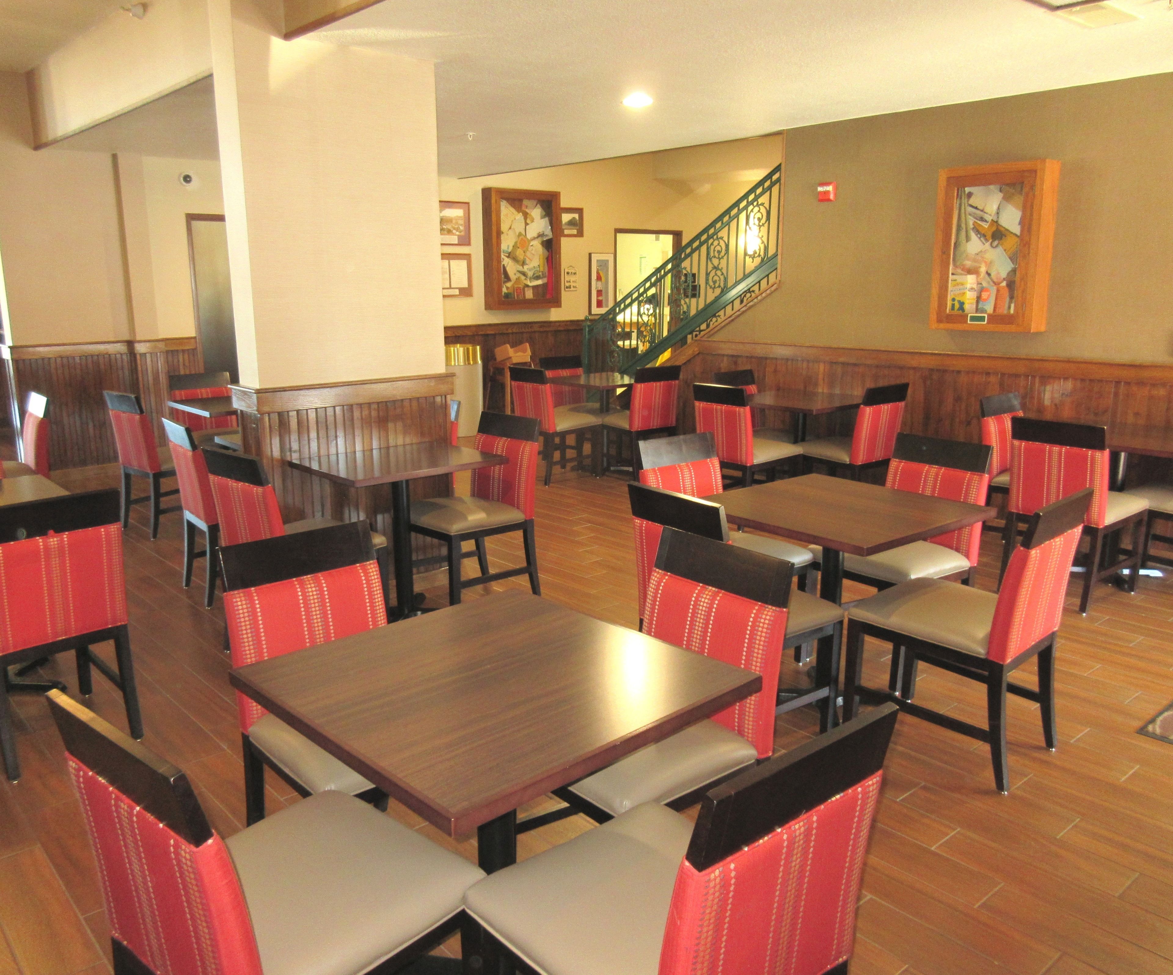 A restaurant with booths and tables, wooden flooring, and a staircase with a railing.