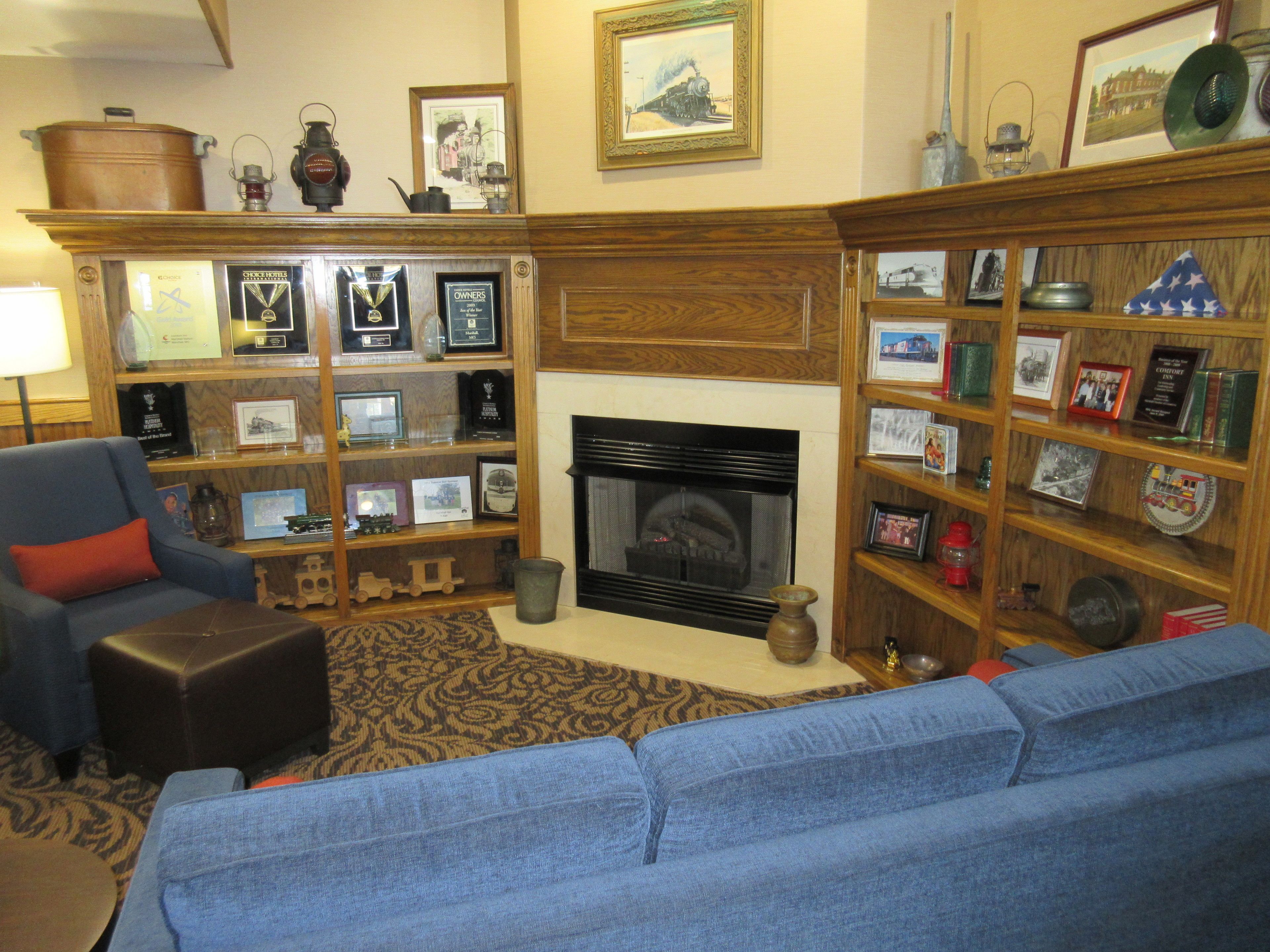 A living room with a fireplace, a blue sofa, and a bookshelf filled with framed pictures and awards.