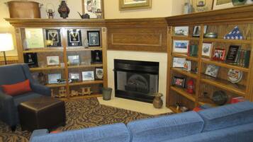A living room with a fireplace, a blue sofa, and a bookshelf filled with framed pictures and awards.