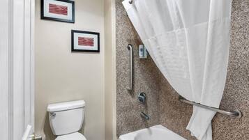 Een badkamer met een toilet, een bad, een douchegordijn en twee ingelijste foto's aan de muur.