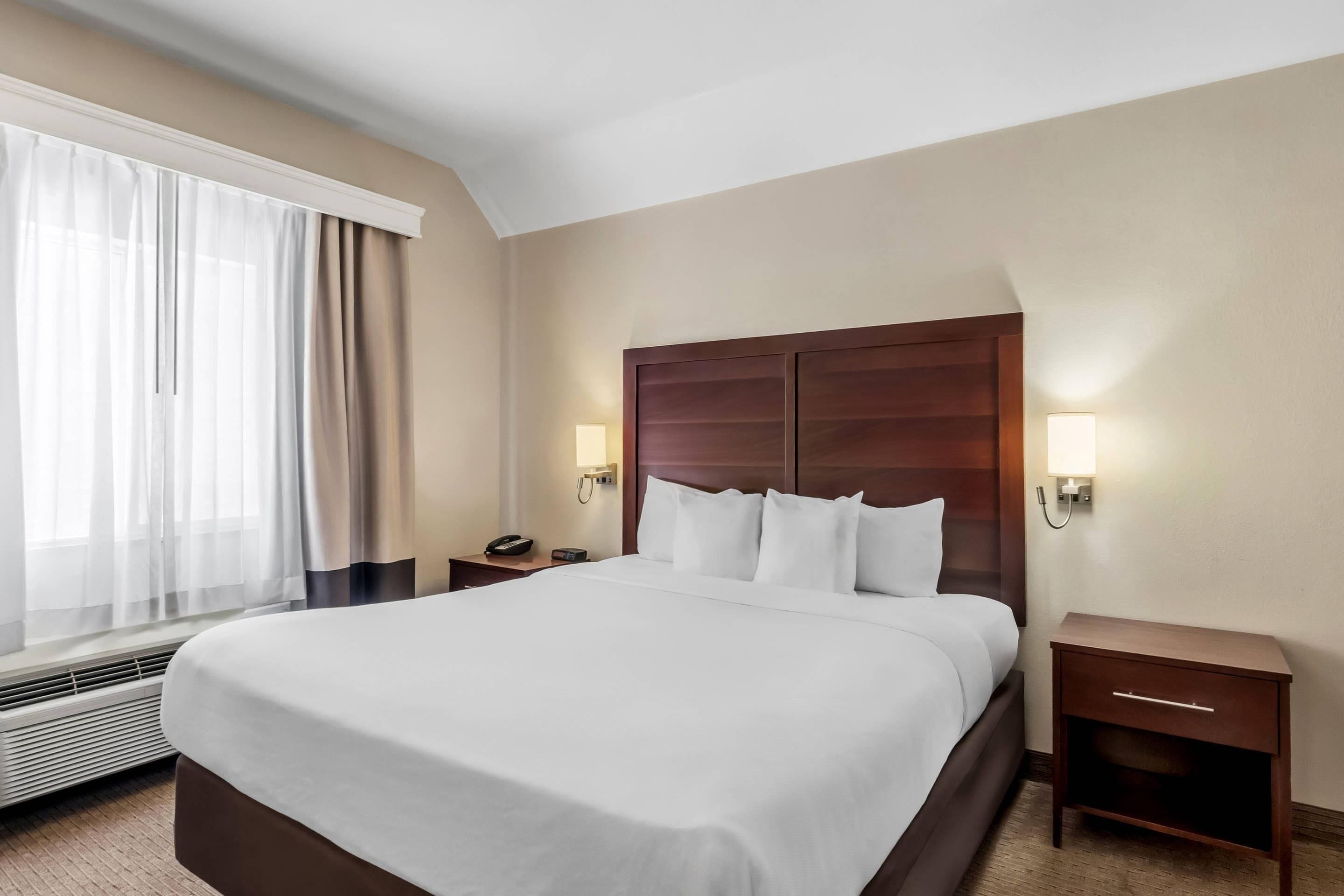 A hotel room with a large bed, two bedside tables, a nightstand, a lamp, and a window with curtains.