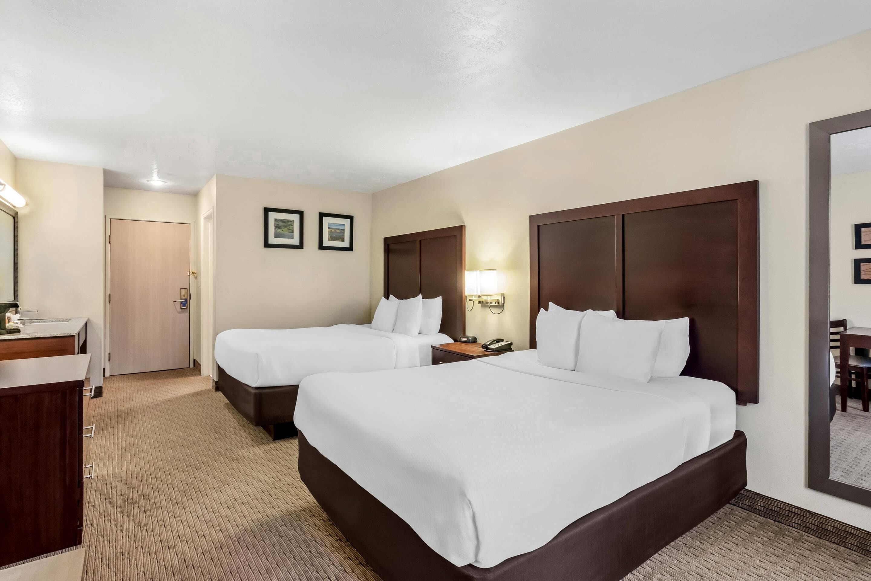 A hotel room with two beds, a desk, a mirror, and a door.