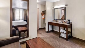 A hotel room with a bed, a sitting area, a wooden table, a mirror, and a bathroom with a sink and towel rack. - Comfort Inn Elko (Elko)