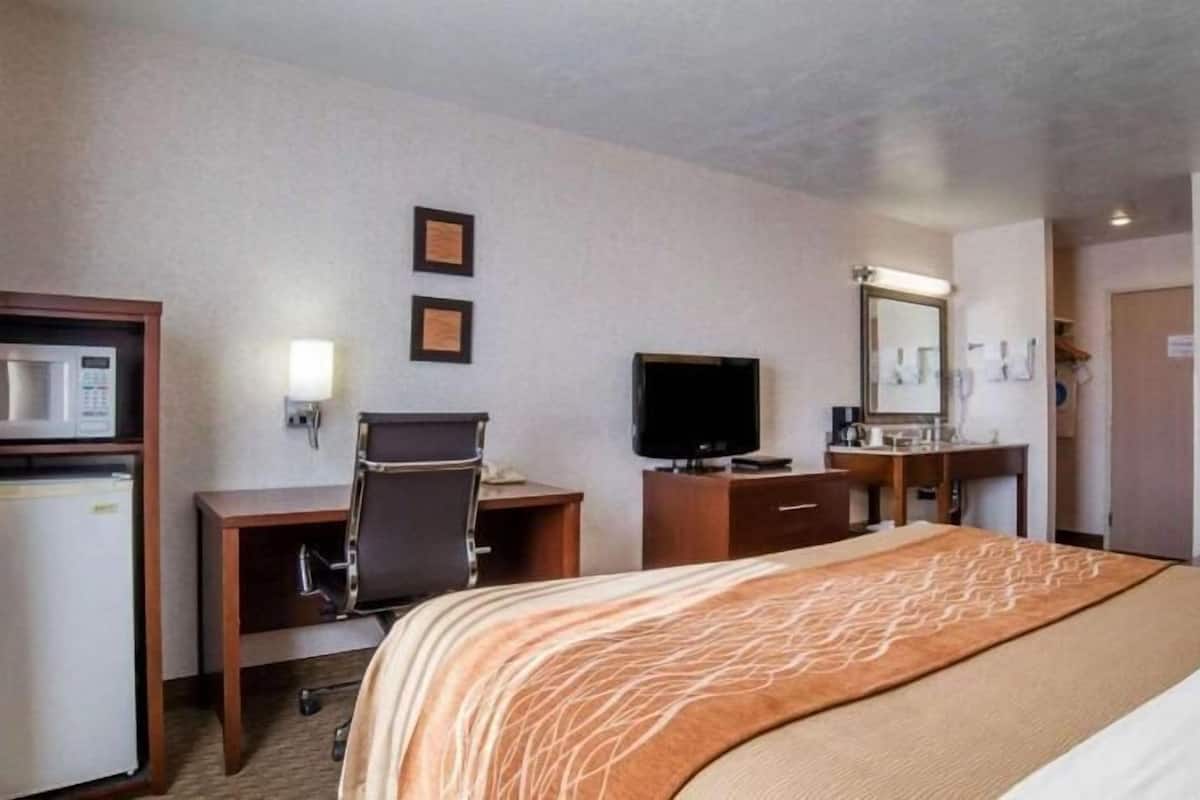 Une chambre d’hôtel équipée d’un lit, d’un bureau, d’une chaise, d’une télévision et d’une salle de bain avec un miroir et un lavabo.