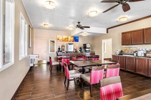 A spacious dining area with multiple tables and chairs, a kitchen area with cabinets and appliances, and a ceiling fan.