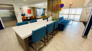 A modern hotel lobby with a central white table, blue chairs, a map on the wall, and a staircase. - Holiday Inn Express Bluffton by IHG (Bluffton)
