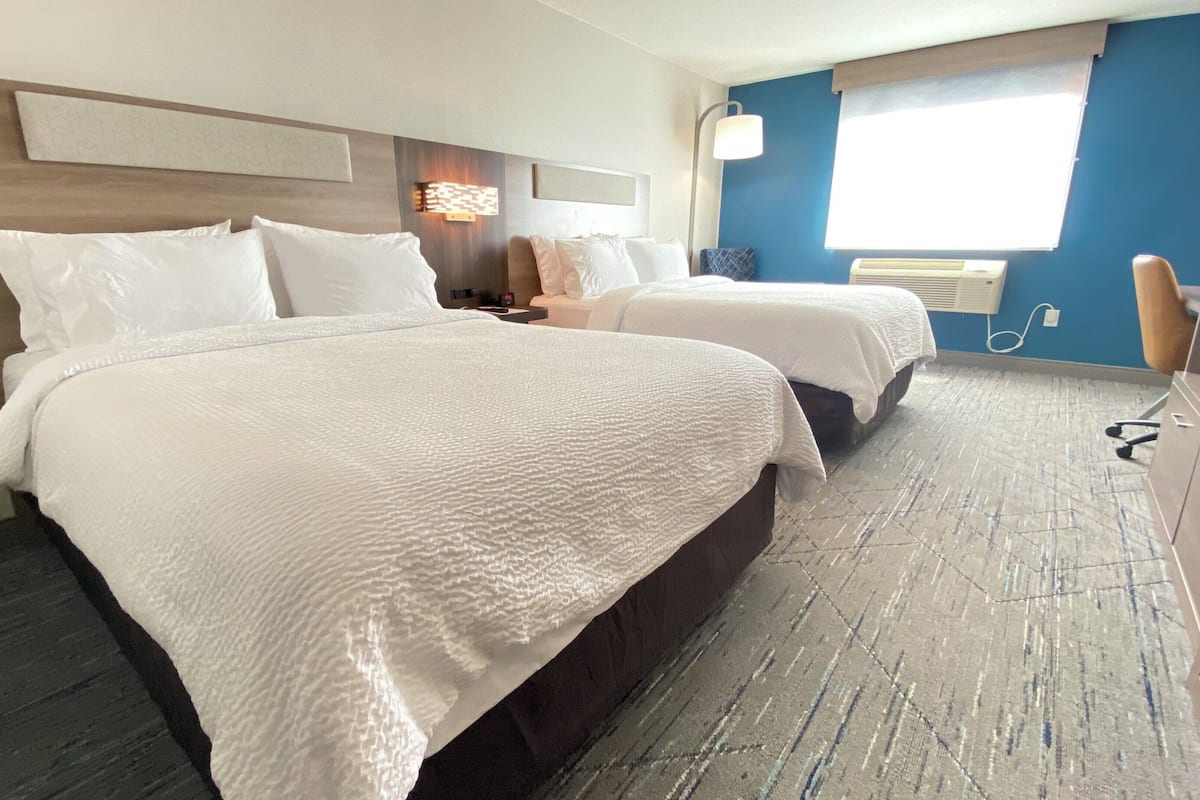 A hotel room with two beds, a desk, a chair, and a window with blinds.