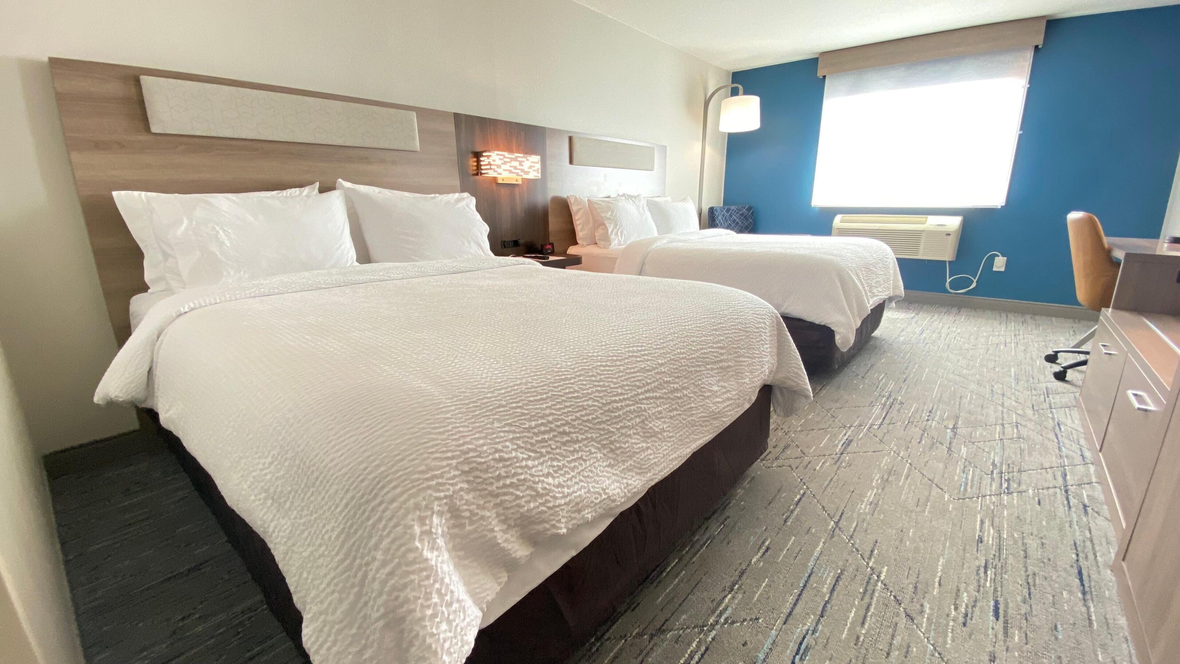A hotel room with two beds, a desk, a chair, a lamp, and a window.