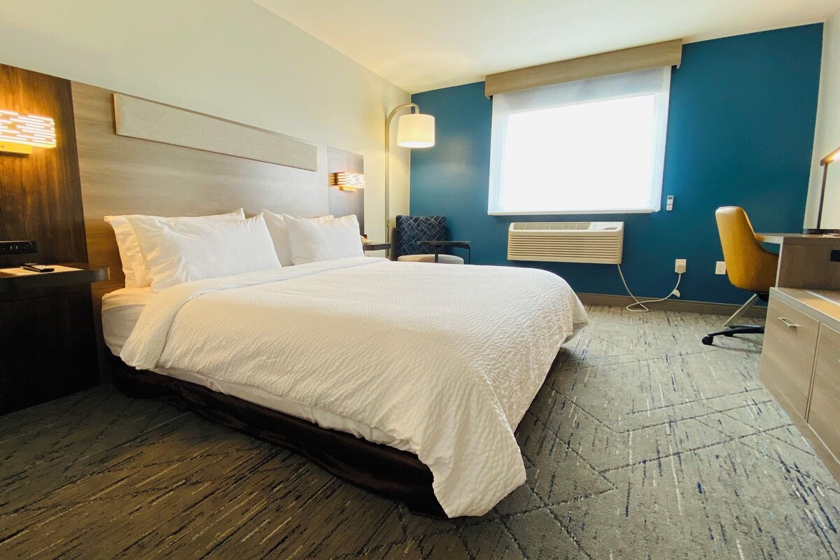 A hotel room with a bed, a desk, a chair, a nightstand, and a window.