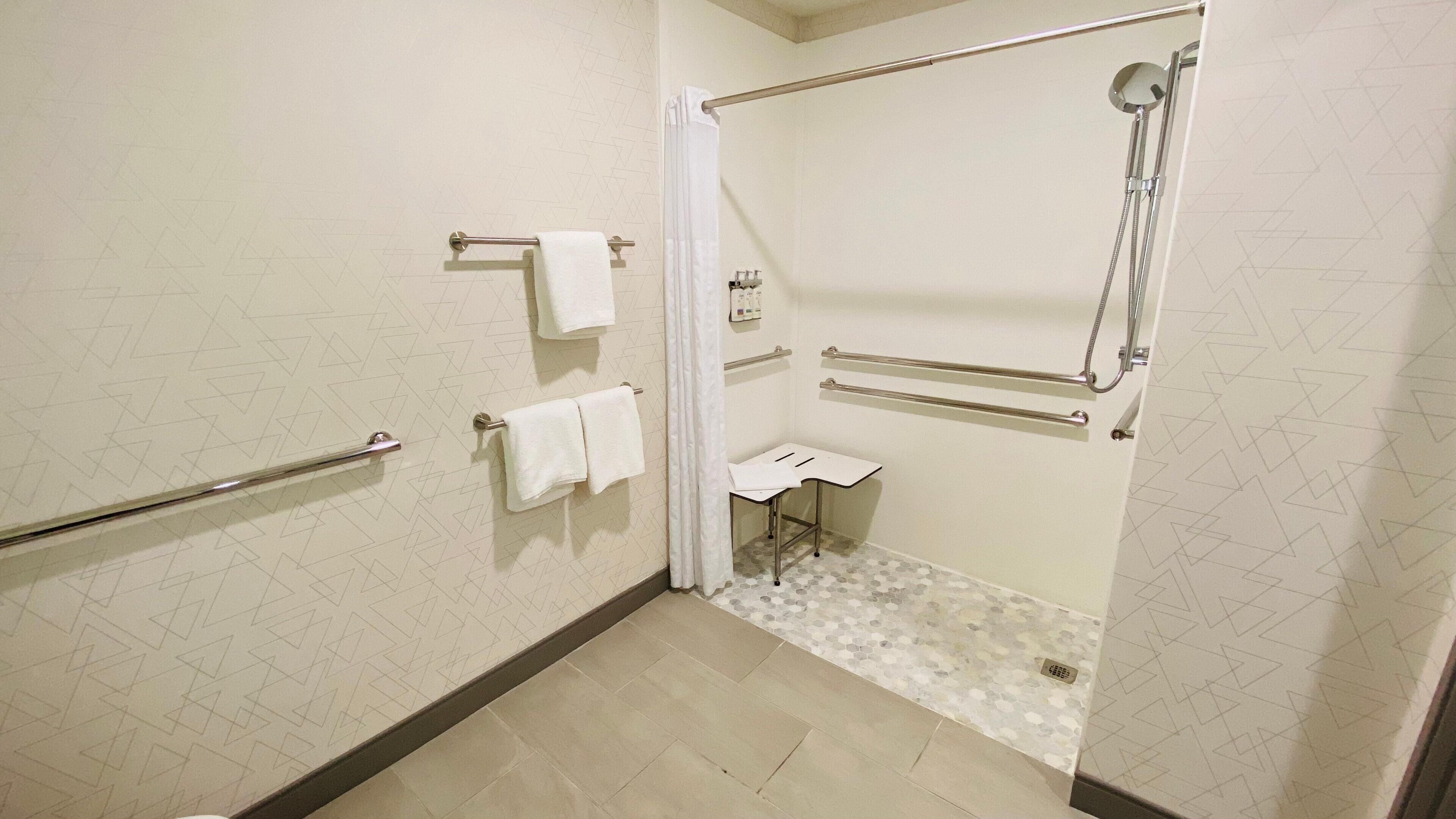 A bathroom with a shower, grab bars, a white sink, and a toilet.