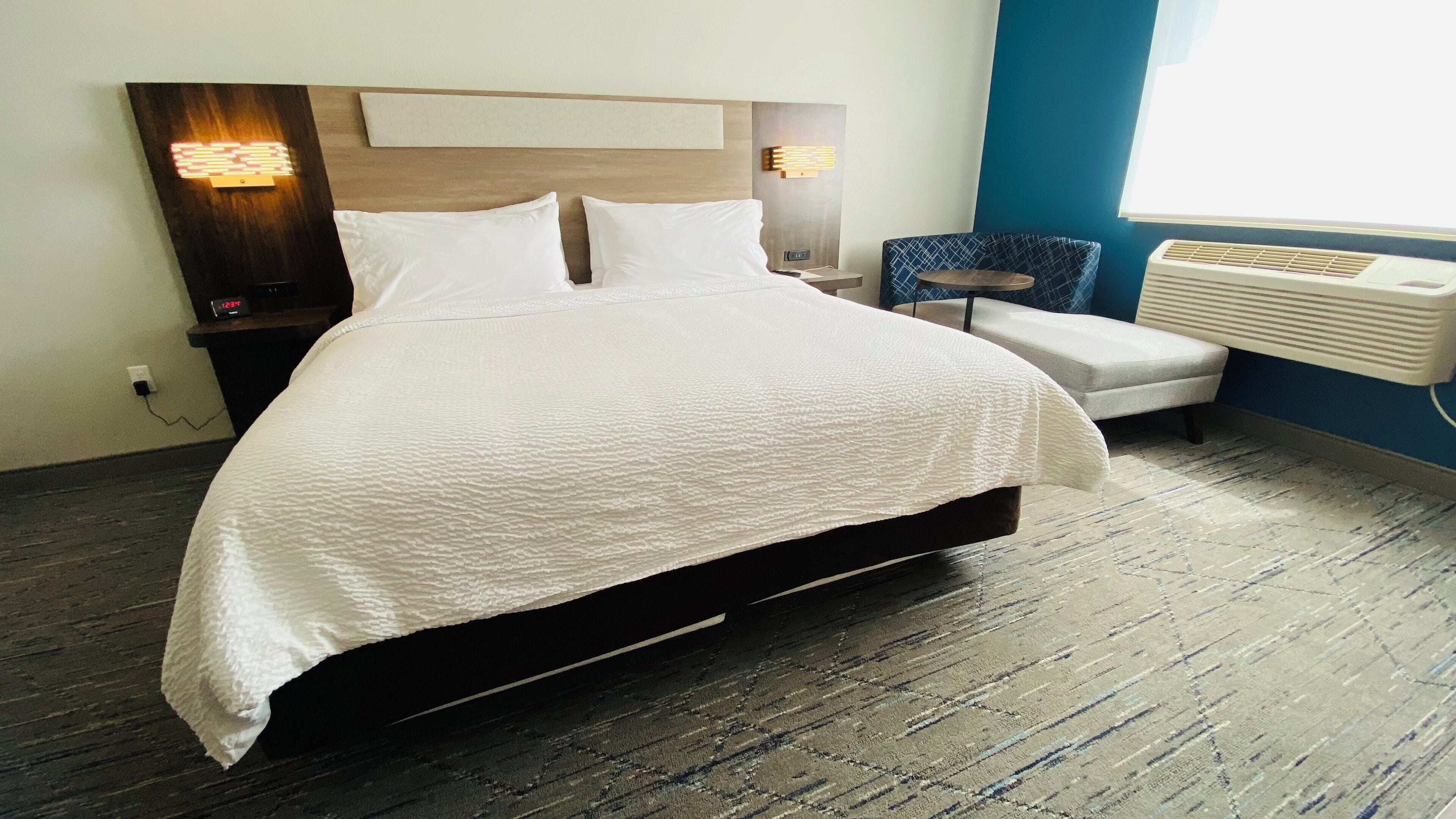 Una habitación de hotel con una cama grande, mesitas de noche, una silla y un radiador.