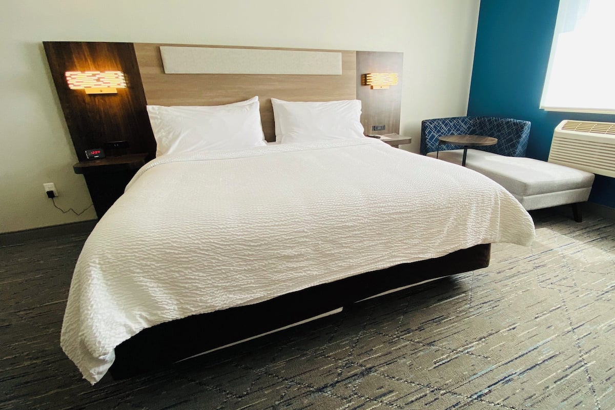 A hotel room with a large bed, bedside tables, a chair, and a radiator.