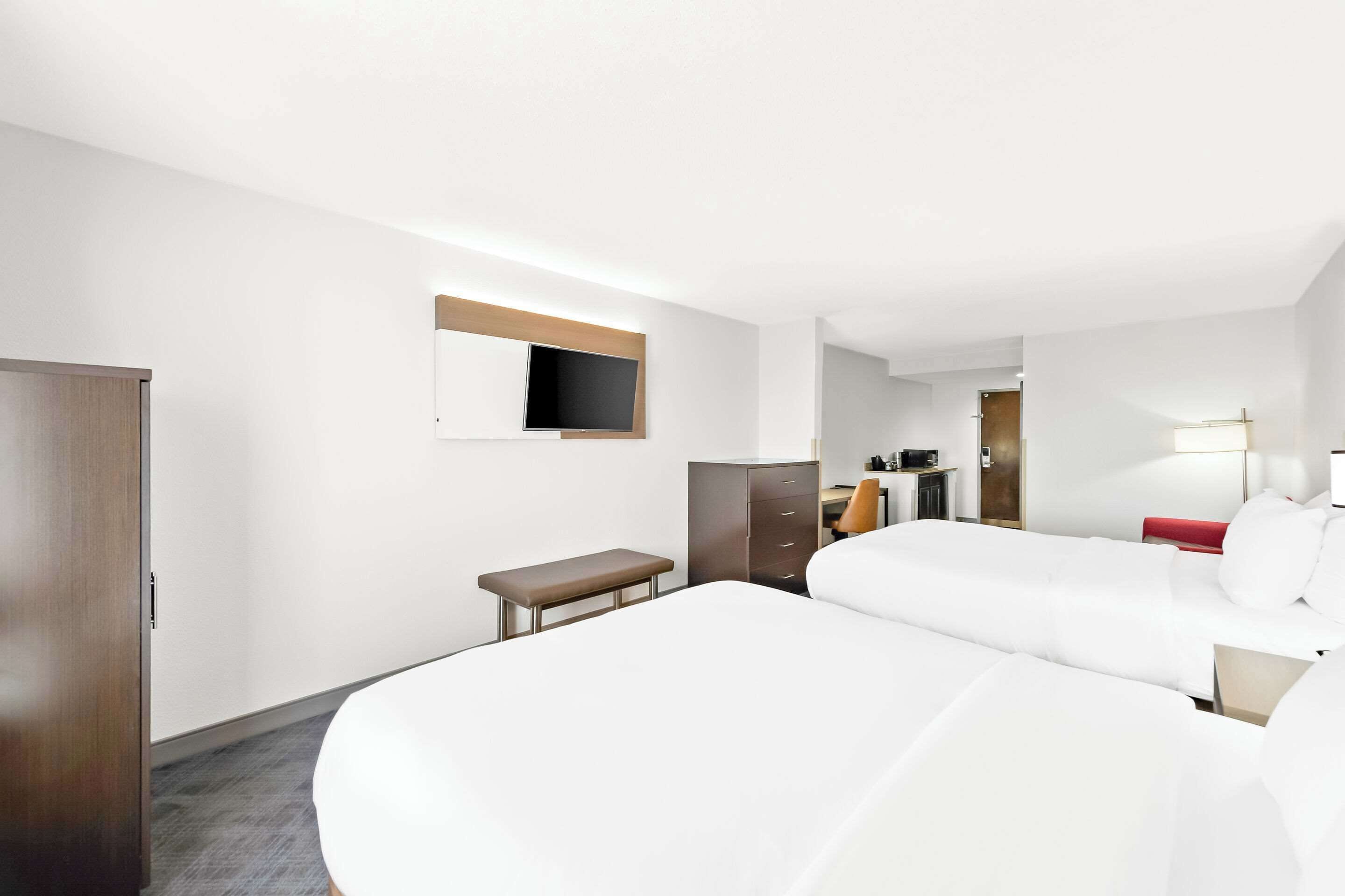 A hotel room with two beds, a desk, a chair, a wardrobe, a TV, and a mirror.