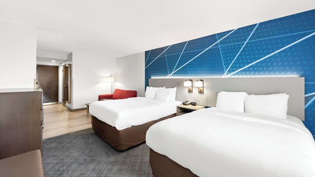 A hotel room with two beds, a red chair, a desk, and a blue geometric wall design. - Comfort Suites Columbus (Columbus)
