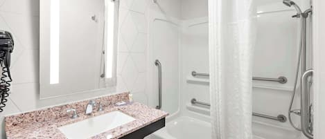A modern bathroom with a granite countertop sink, a large mirror, a shower with grab bars, and a towel rack.