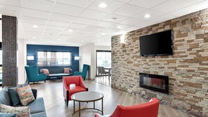 A modern lounge area with seating, a fireplace, and a large flat-screen TV mounted on a stone wall. - Comfort Suites Columbus (Columbus)