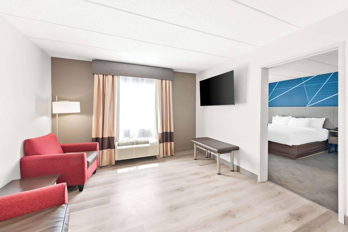 A hotel room with a bed, a desk, a chair, a TV, and a window with curtains.