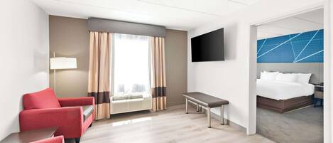 Habitación de hotel con cama, escritorio, silla, televisor y ventana con cortinas.