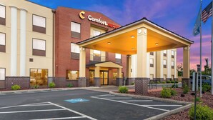 A Comfort Suites hotel with a covered entrance, a parking lot, and a landscaped area with shrubs. - Comfort Suites Columbus (Columbus)