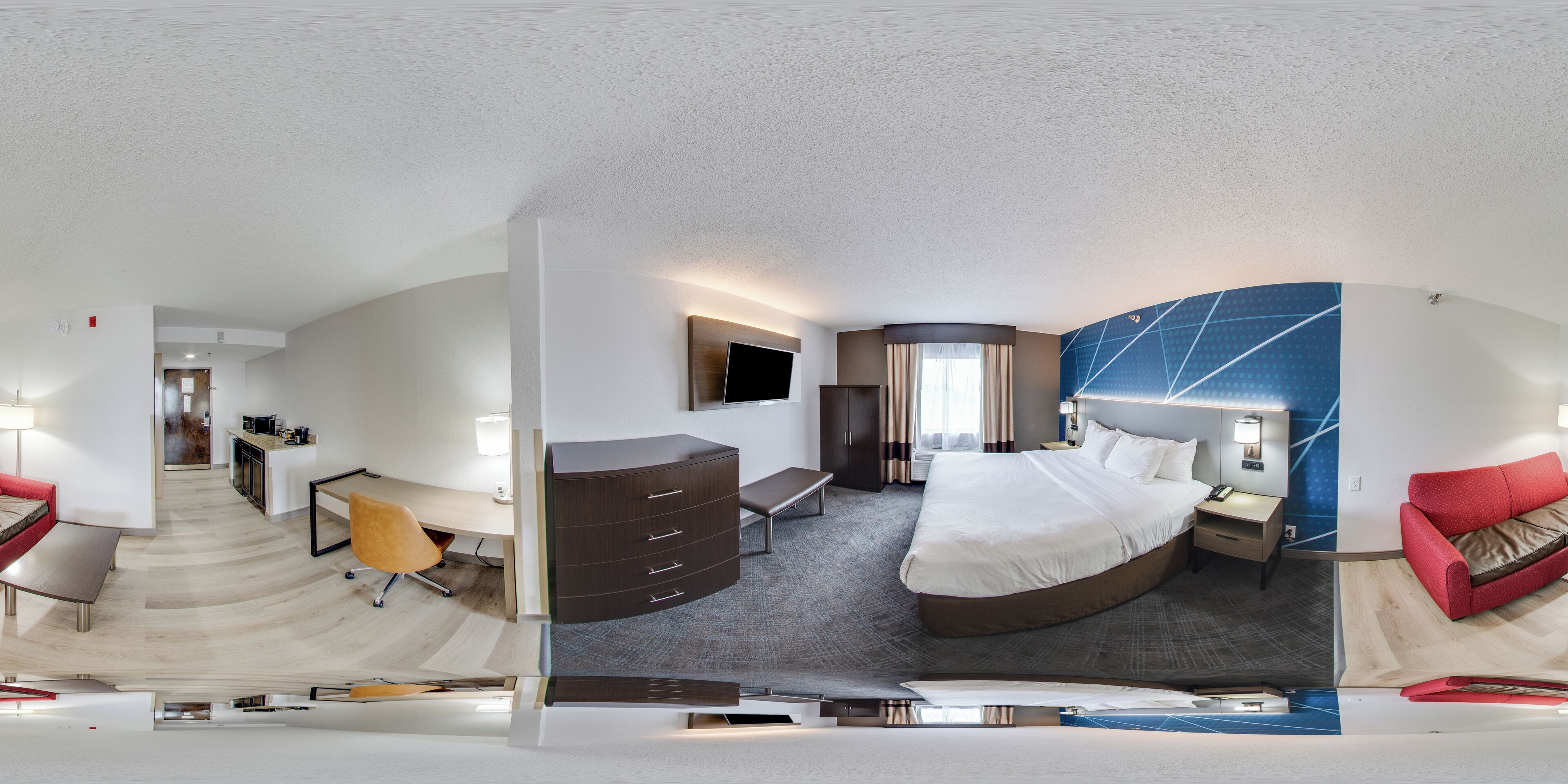 A modern hotel room with a curved bed, a desk, a chair, a wardrobe, and a TV.