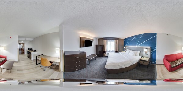 A modern hotel room with a curved bed, a desk, a chair, a wardrobe, and a TV.