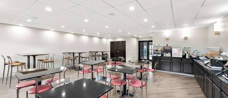 Un comedor amplio con varias mesas y sillas, una encimera de cocina y un interior moderno y limpio.
