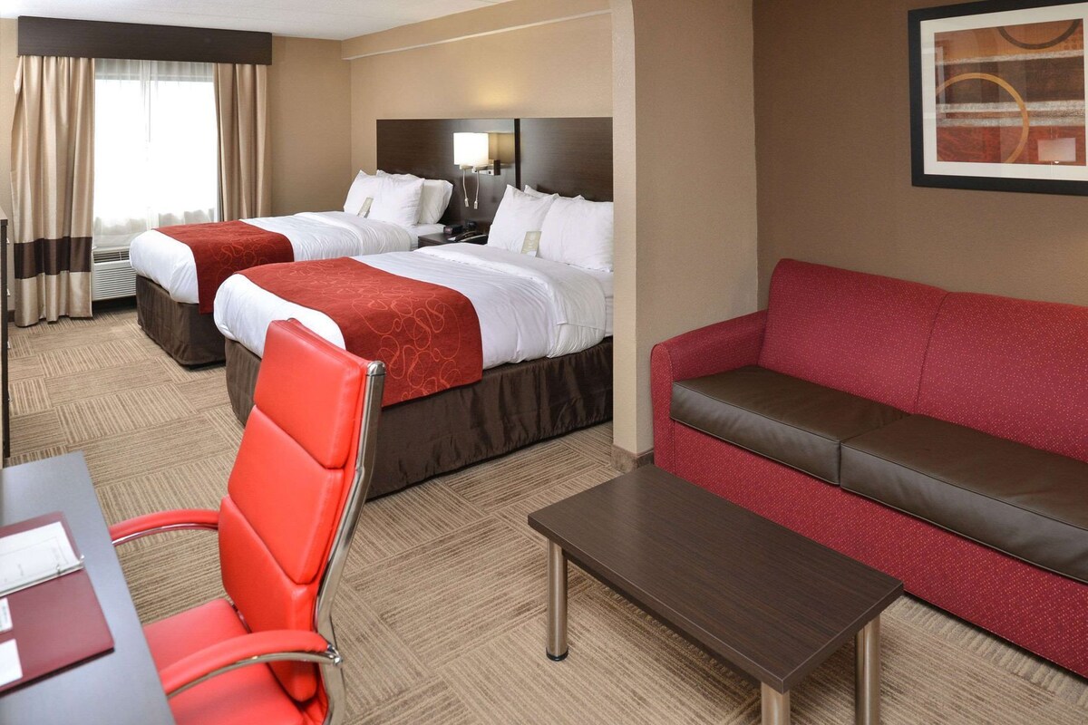 A hotel room with two beds, a red sofa, a red chair, and a small table.