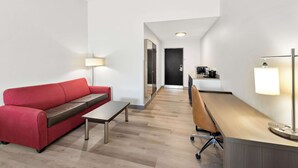 A modern hotel room with a red sofa, a wooden desk, and two lamps. - Comfort Suites Columbus (Columbus)