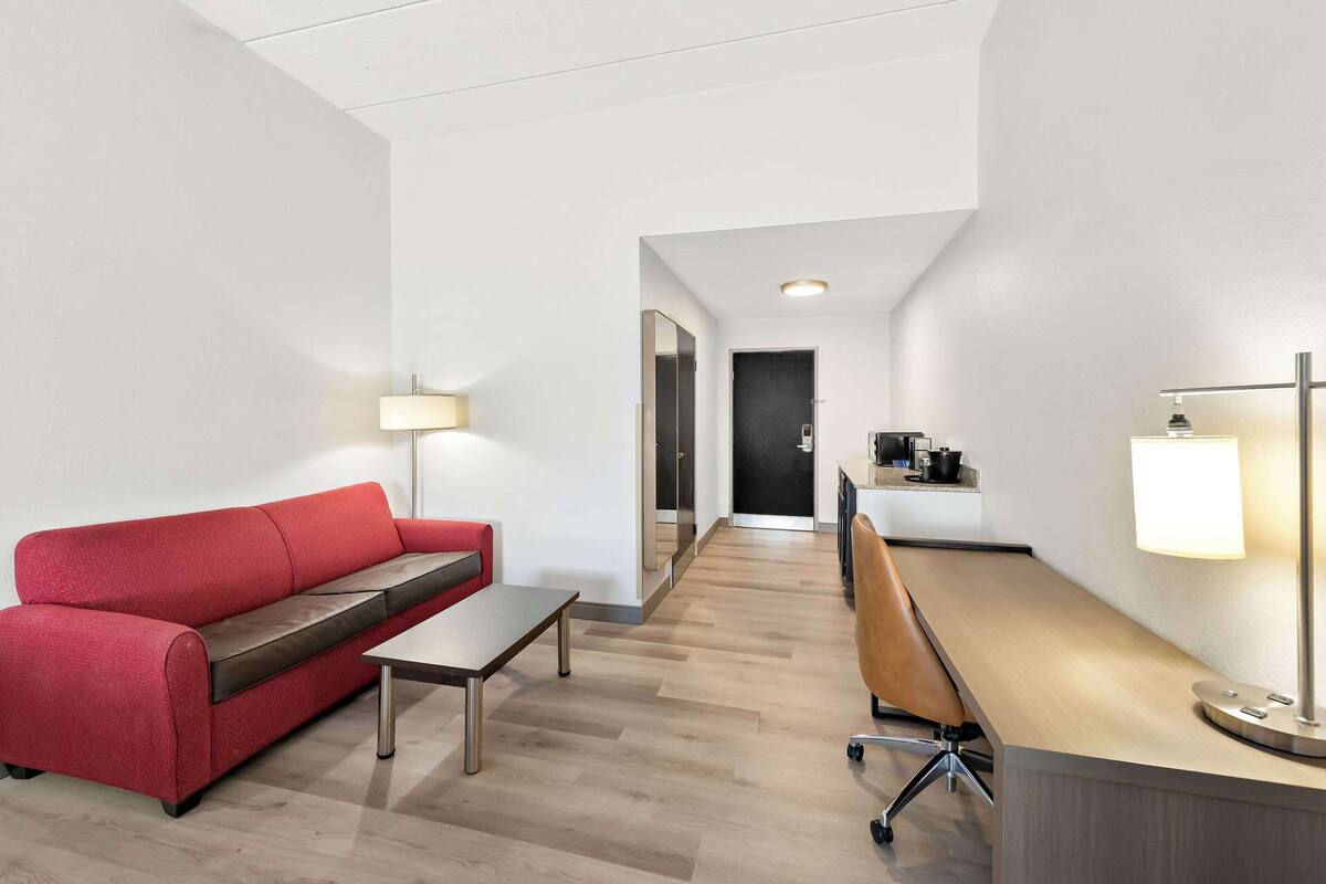 A modern hotel room with a red sofa, a wooden desk, and two lamps.