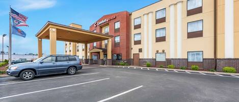 A hotel with a covered entrance, a parking lot, and a flag.