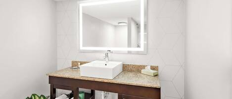 A modern bathroom with a white sink, a large mirror, and a granite countertop.