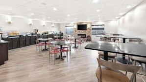 A modern dining area with tables and chairs, a kitchen area, and a stone fireplace. - Comfort Suites Columbus (Columbus)