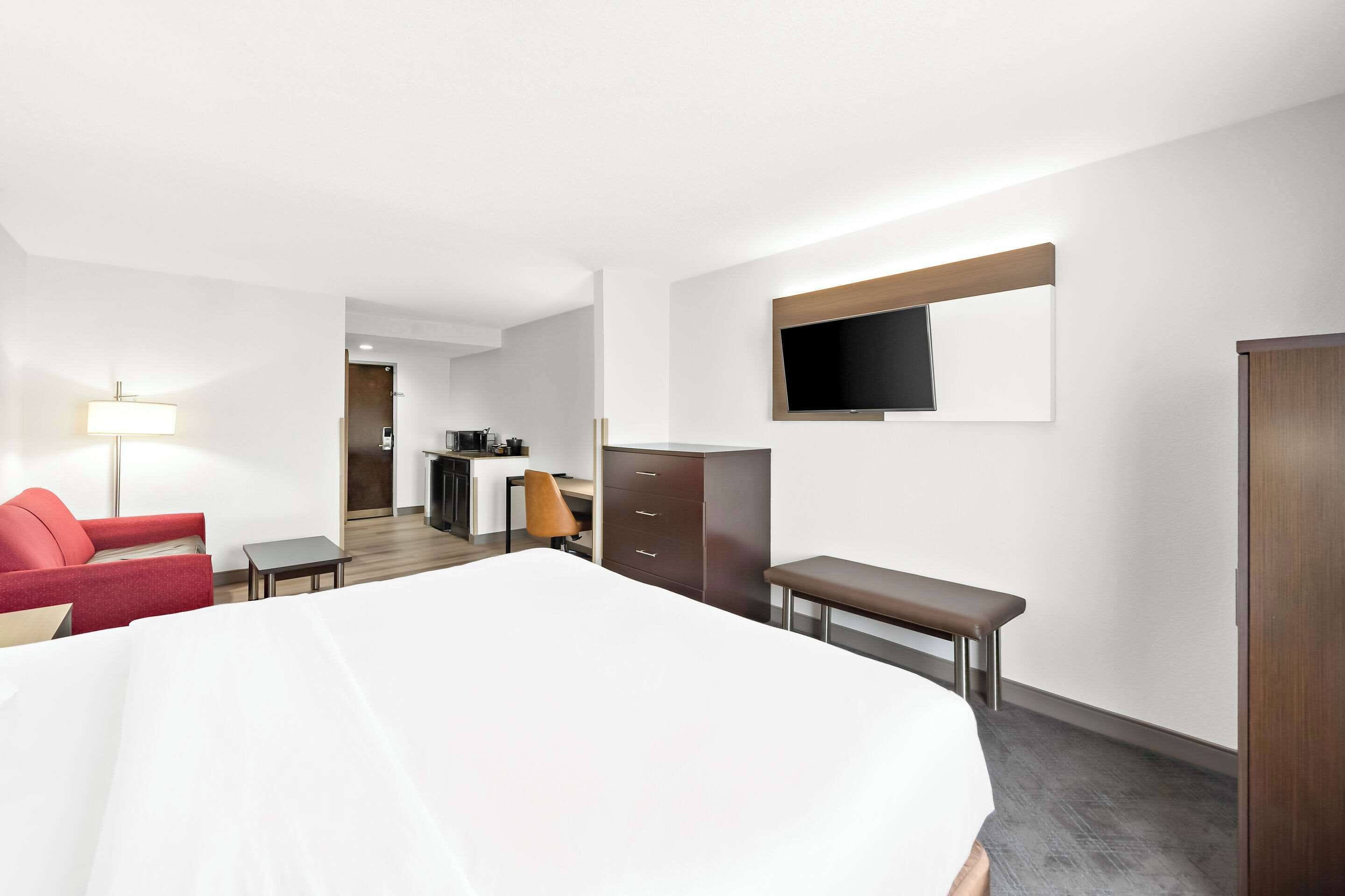 Una camera d'albergo con un letto, un divano rosso, una scrivania, una televisione e un armadio.