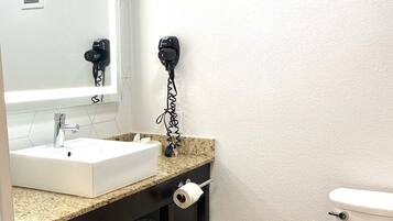 Un baño con lavamanos blanco, un espejo, secador de pelo, inodoro y toallero con toallas.