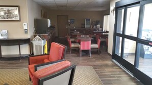 A hotel lobby with a seating area, a reception desk, and a view through large windows. - Cambridge Inn by Capital O near I-70 / I-77 (Cambridge)