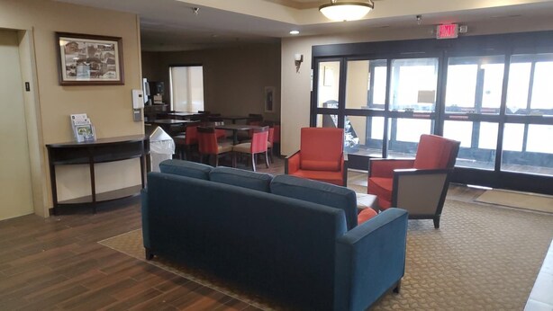 A lobby with a blue sofa, red chairs, a reception desk, and a large window offering a view. - Cambridge Inn by Capital O near I-70 / I-77 (Cambridge)