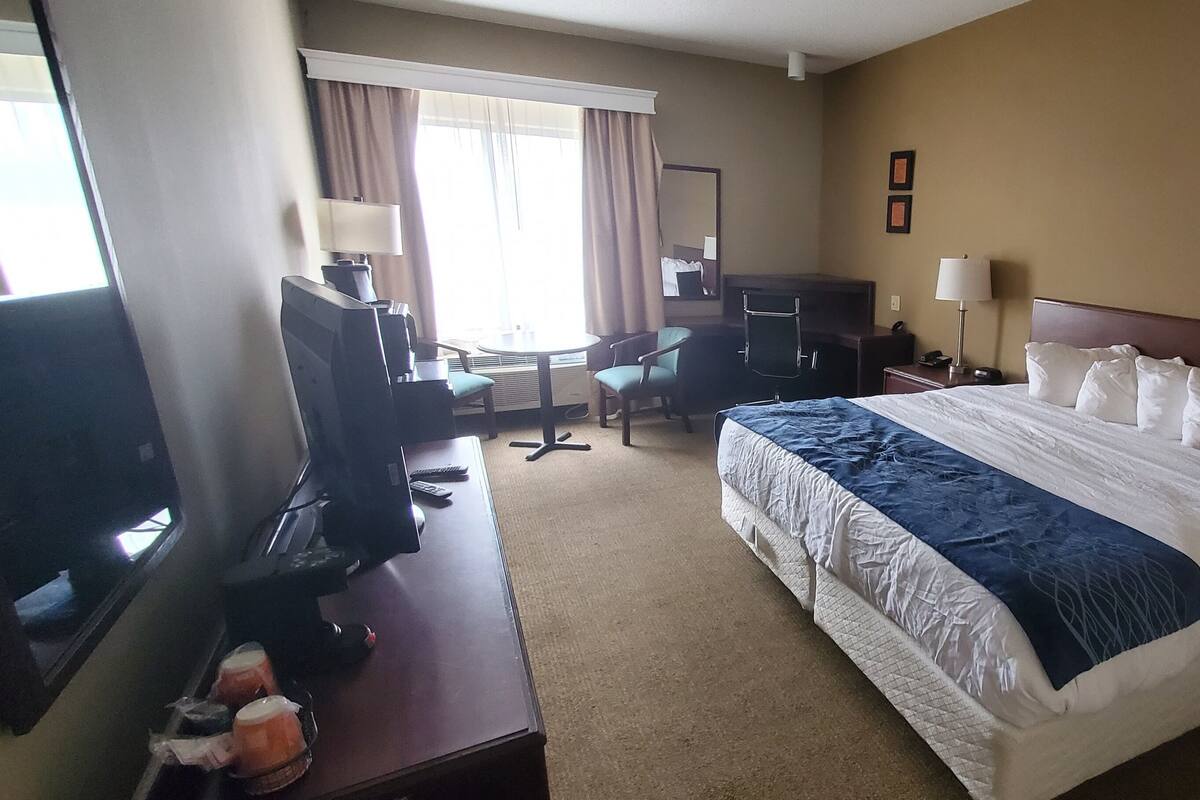 A hotel room with a bed, desk, chair, TV, and a window with curtains.