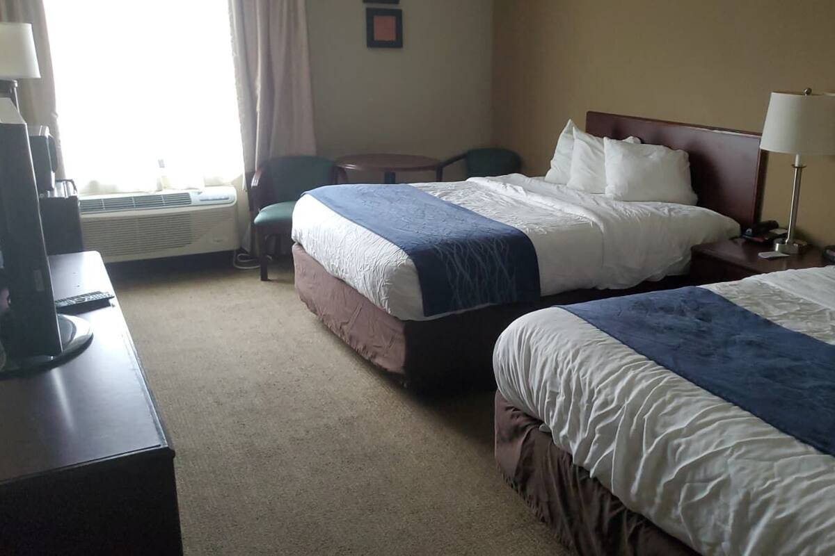 A hotel room with two beds, a desk with a computer, a chair, and a small table.
