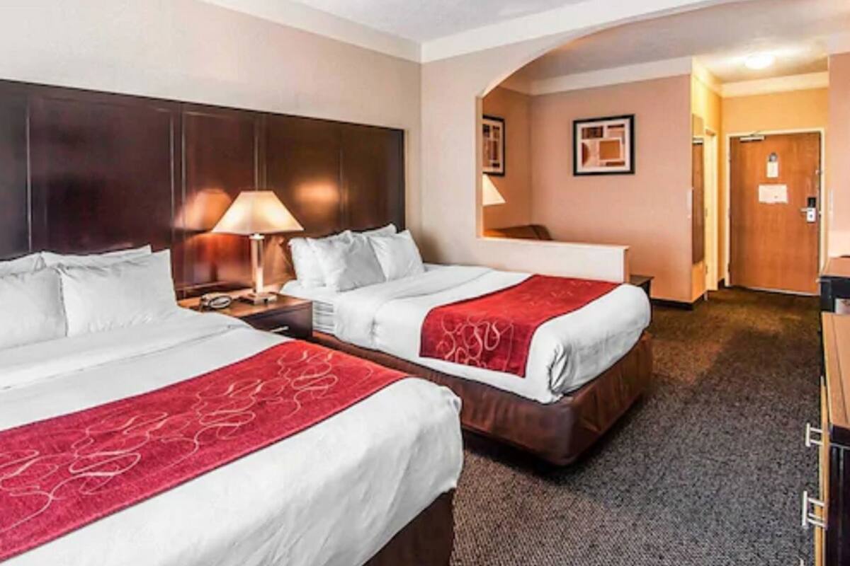 A hotel room with two beds, a desk, a chair, and a door.