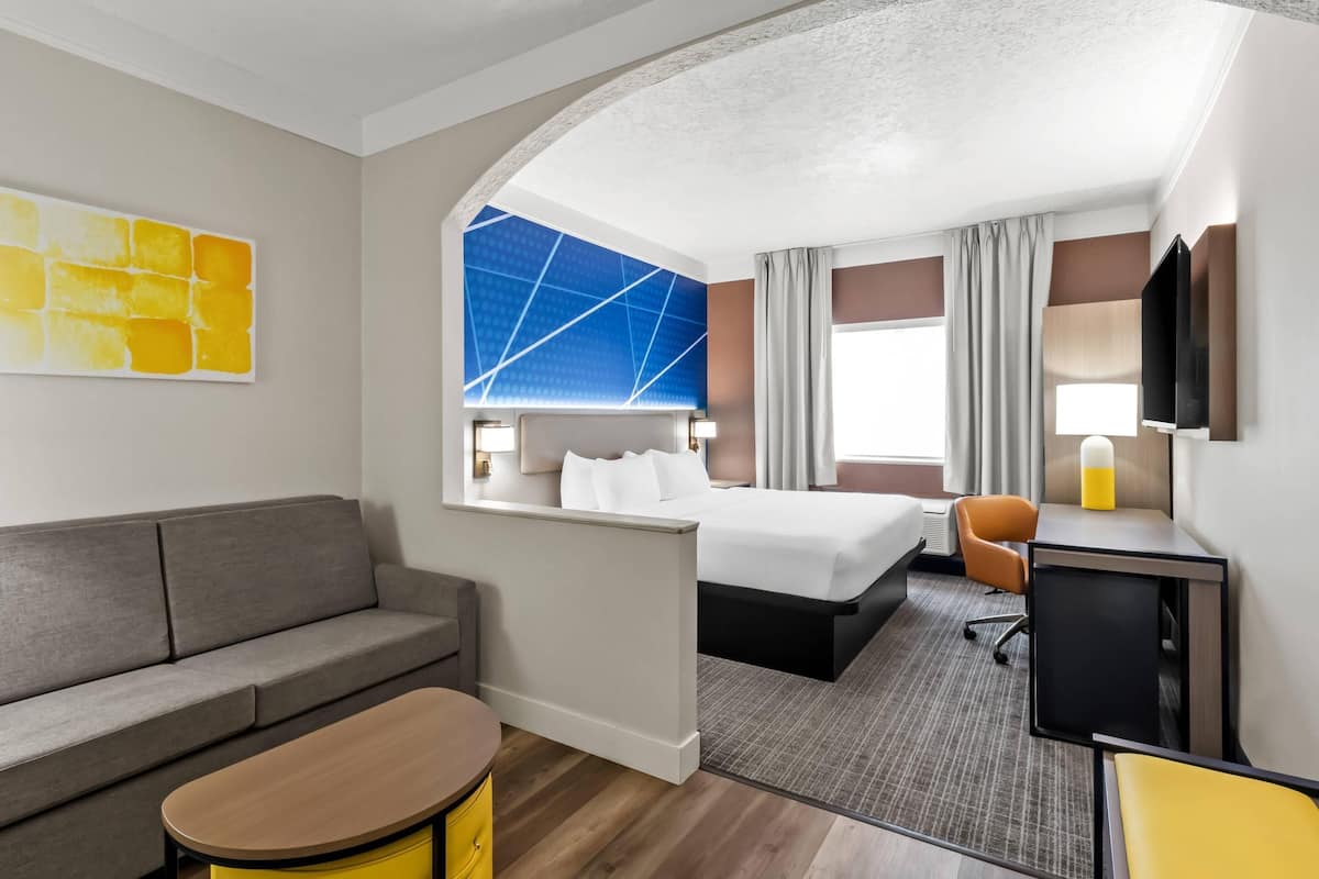 A hotel room with a bed, a sofa, a desk, and a TV.