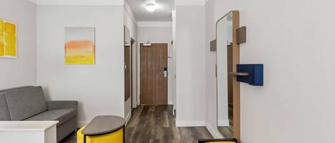 Une chambre d’hôtel moderne avec un canapé gris, un pouf jaune, une petite table et un banc.