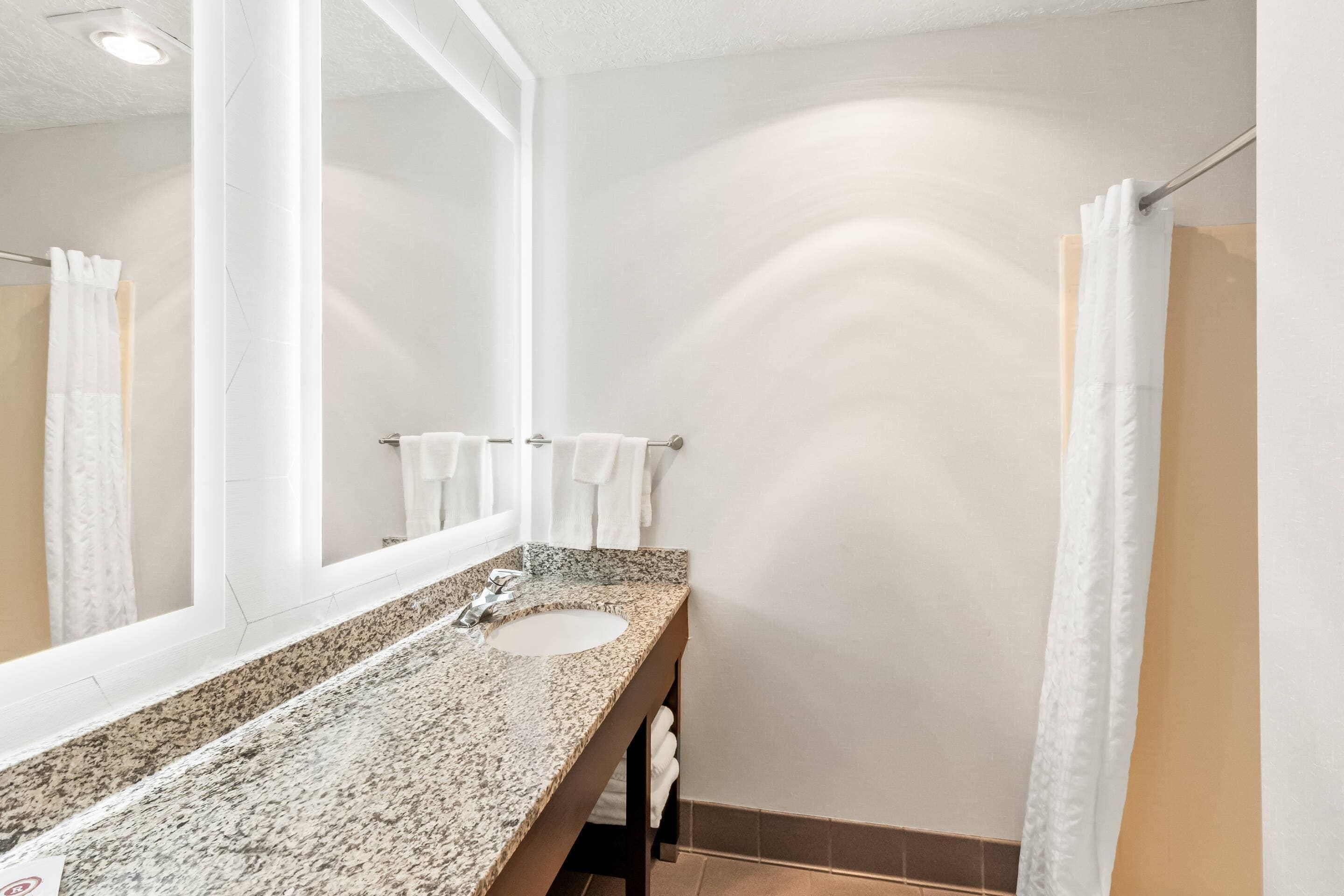 A bathroom with a granite countertop sink, a large mirror, and white towels hanging on the wall.